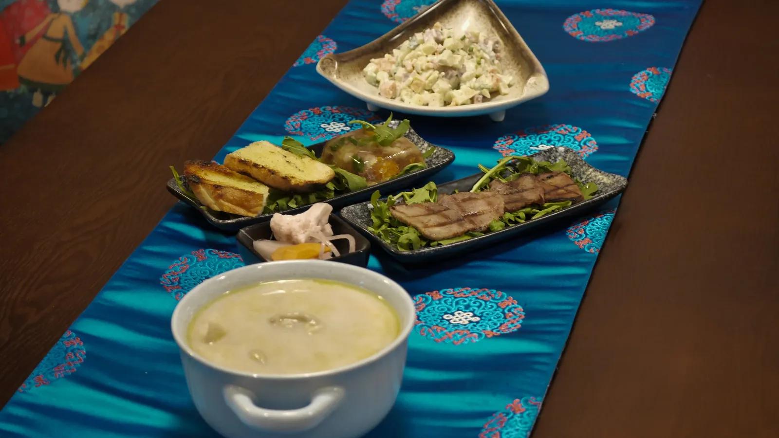 A table laid along a blue Mongolian runner with soup, salads and grilled tongue