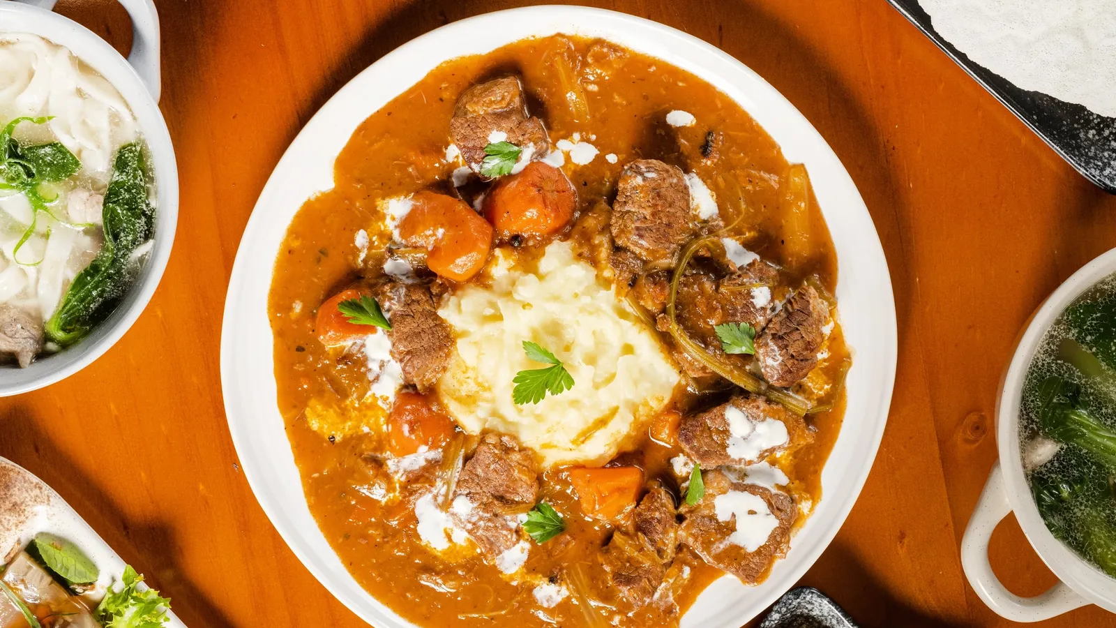 Overhead view of a shared table: beef goulash, noodle soups, salads and flatbread